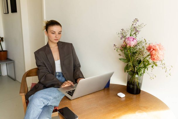 Giovane donna che utilizza laptop vicino smartphone e fiori a casa  - Foto, immagini