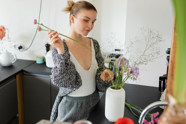 Woman in warm cardigan making floral bouquet in vase at home  - Φωτογραφία, εικόνα