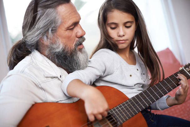 Ik krijg gitaartips van een doorgewinterde muzikant. een klein meisje speelt gitaar met haar grootvader - Foto, afbeelding
