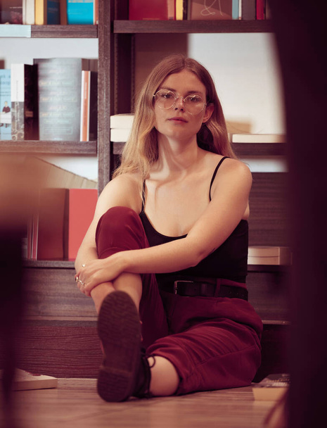 Woman, gen z and library shelf with a college student relax on a study hall or room floor. Portrait of a person with books in an education, knowledge and university center looking calm and casual. - Zdjęcie, obraz