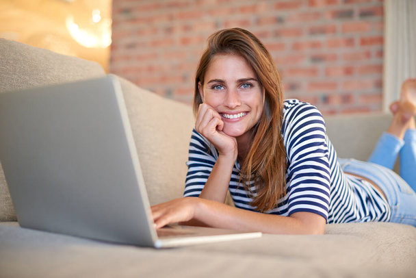 Laptopumla tembellik ediyorum. Evdeki kanepesinde dizüstü bilgisayar kullanan genç bir kadın. - Fotoğraf, Görsel