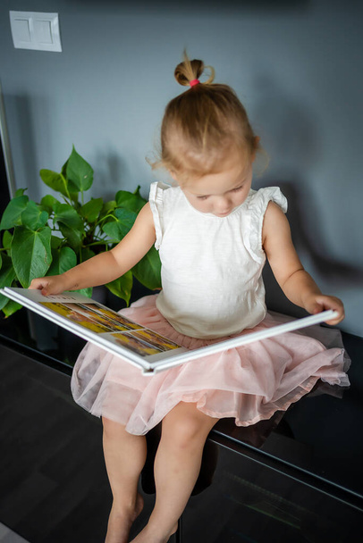 Happy cute little girl looking at photos in album. Happy smiling daughter browsing through printed family album, looking at pictures. High quality photo - Valokuva, kuva