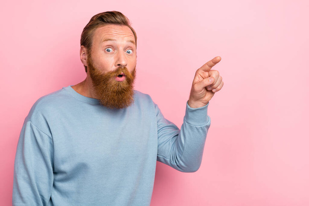 Portrait of positive impressed astonished man with red beard dressed blue sweater directing empty space isolated on pink color background. - Fotografie, Obrázek