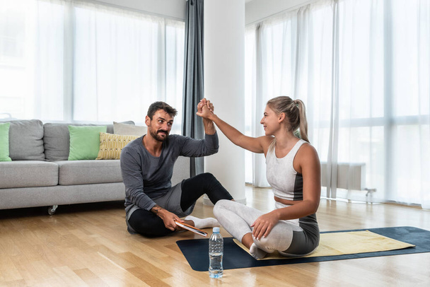 Young fitness and yoga instructor working in your home. Sporty educated coach therapist man helping young woman at recovery in her apartment and home in workout and training for healthy life. - Foto, Bild