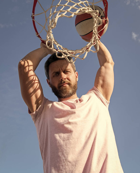 guy has sport motivation. sport and hobby. dunk in basket. slam dunk in motion. summer activity. bearded man with basketball ball on court. professional basketball player training outdoor. - Photo, Image