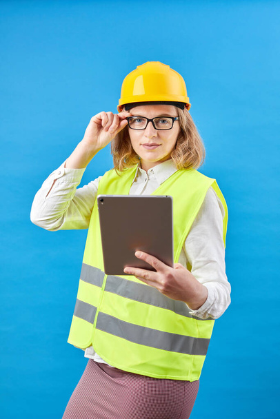 Business woman builder working with tablet PC. Usmívající se žena ve studiu na modrém pozadí. Koncept výstavby, opravy, dekorace - Fotografie, Obrázek