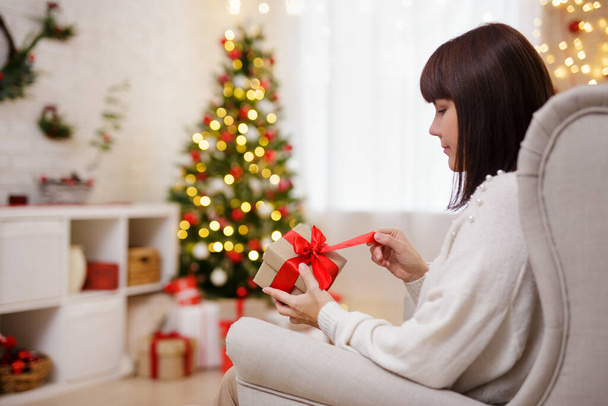 Nainen istuu nojatuoli ja avoin lahja joulu sisustettu huone - Valokuva, kuva