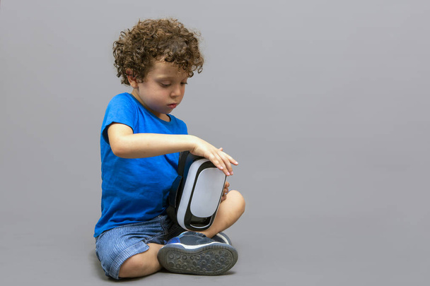niño pequeño con gafas de realidad virtual en sus manos mirando curiosamente cómo funcionan - Foto, imagen