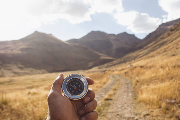 Hält einen Kompass auf dem Hintergrund einer Bergstraße - Foto, Bild