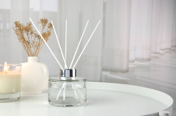 luxury aroma scent reed diffuser glass bottle is on white steel table with clear glass of scented candle and vase to creat romantic and relax ambient with background of nice white curtain in bedroom  - Foto, afbeelding
