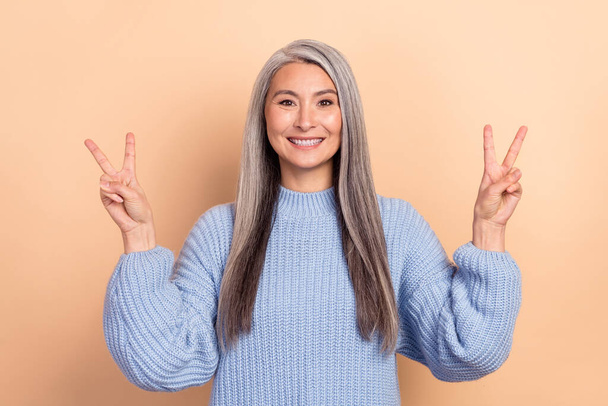 Photo of good mood laughing positive mature woman showing v-sign say hi isolated on beige color background. - Фото, изображение
