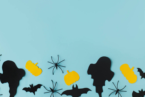 Happy Halloween. Black ghosts, spiders, bats and yellow pumpkins decorations on blue background flat lay. Creative Card template with space for text. Modern minimal border - Фото, изображение