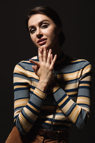 young woman in striped turtleneck looking at camera isolated on black  - Foto, Imagem