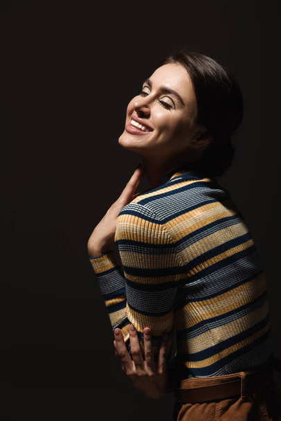 cheerful young woman in striped turtleneck smiling isolated on black  - Photo, Image