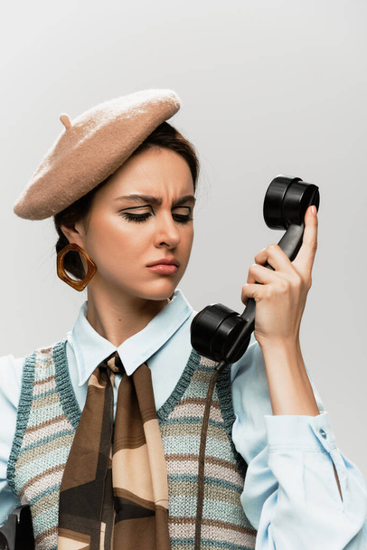 niezadowolona młoda kobieta w berecie rozmawia przez telefon vintage odizolowany na szarości  - Zdjęcie, obraz
