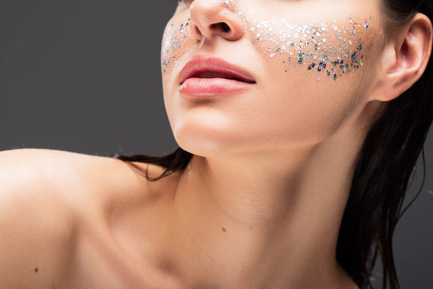 cropped view of young woman with sparkling glitter on cheeks isolated on grey - Fotó, kép