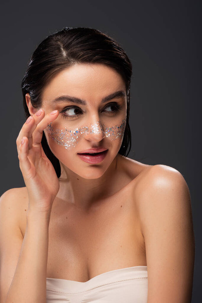 pretty young woman with bare shoulders and sparkling glitter on cheeks isolated on grey - Photo, Image