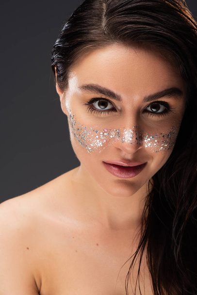 young brunette woman with natural makeup and sparkling glitter on cheeks looking at camera isolated on grey - Foto, Bild