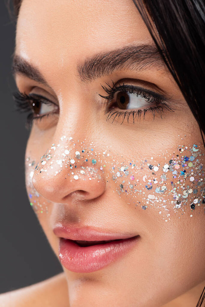 close up of young brunette woman with shiny glitter on cheeks isolated on grey  - Foto, imagen