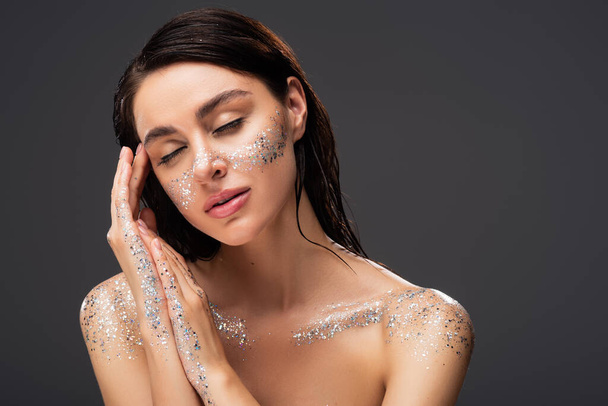 portrait of sleepy woman with sparkling glitter on cheeks and hands isolated on grey  - Фото, зображення