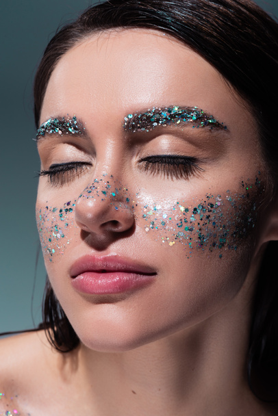 portrait of young woman with glitter on cheeks and eyebrows isolated on grey  - Foto, Imagem