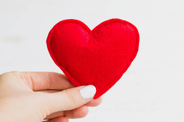 La mano femenina sostiene un corazón rojo sobre un fondo blanco. Concepto de San Valentín - Foto, imagen