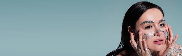 muotokuva brunette nainen glitter posket ja kulmakarvat koskettaa kasvoja katsellen pois eristetty harmaa, banneri - Valokuva, kuva