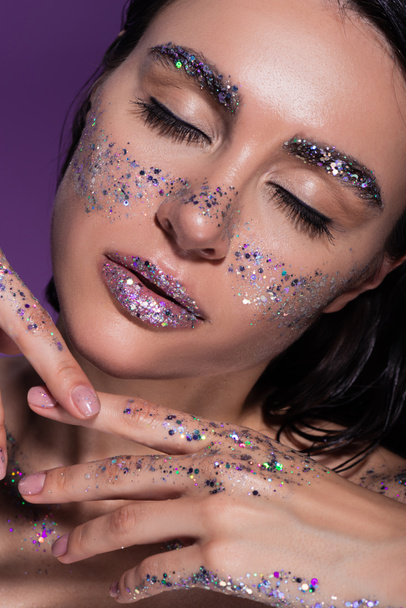 portrait of young woman with closed eyes and glitter on face isolated on purple - Фото, изображение