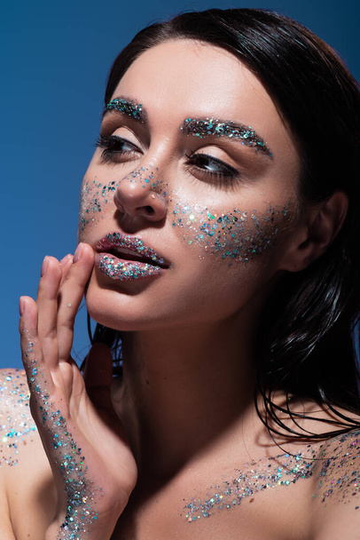 portrait of brunette young woman with glitter on lips and cheeks isolated on blue  - Foto, immagini