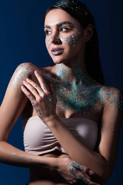 portrait of brunette young model with glitter on body and cheeks isolated on blue  - Foto, immagini
