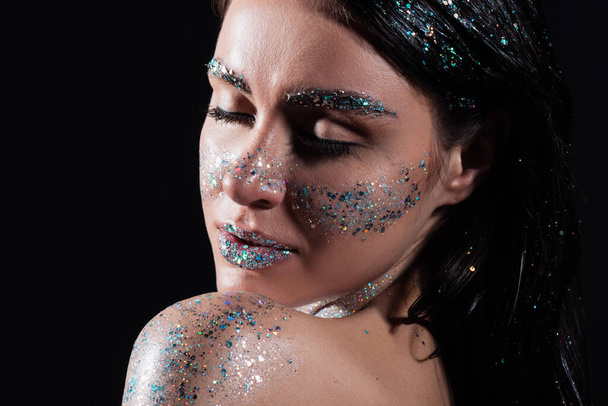 portrait of young woman with closed eyes and sparking glitter on body isolated on black - Foto, imagen