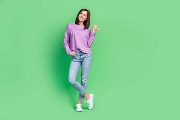 Full length photo of young gorgeous funny girl smiling toothy finger directing empty space recommend new shopping mall isolated on green color background. - Valokuva, kuva