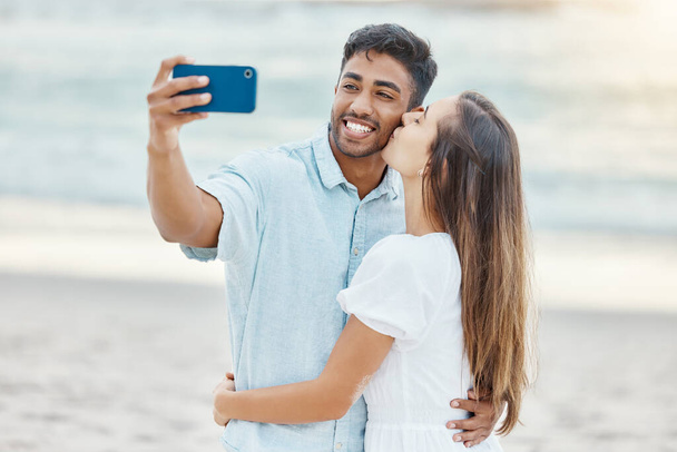 Travel, vacation and selfie by couple kiss on a beach holiday, bonding and having fun on seaside getaway. Young man and woman embrace, enjoying their relationship and romance on a romantic trip. - Fotografie, Obrázek
