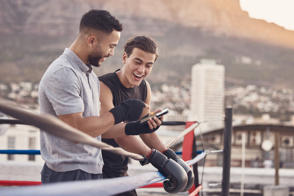 Boxer and coach with phone after training, exercise or workout reading social media meme online. Sport athlete smile and laugh after coaching mma, muay thai and boxing outdoor in a fighting ring. - Photo, image