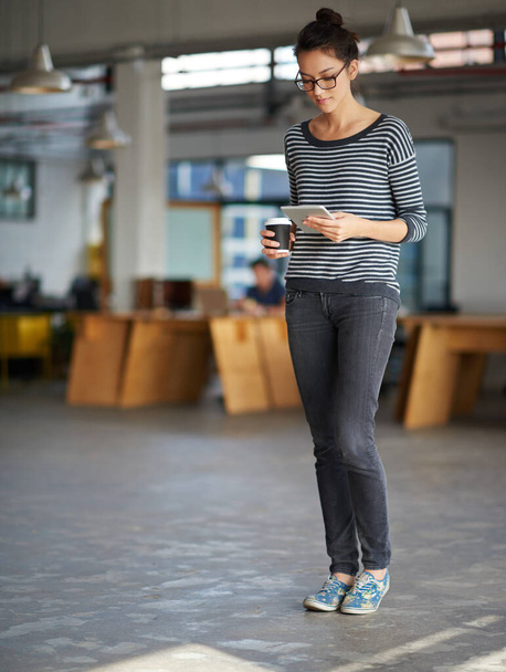 Technici ji udržují v kontaktu. Mladá žena drží odnášející kávu a dívá se na svůj digitální tablet v otevřené kanceláři plánu - Fotografie, Obrázek