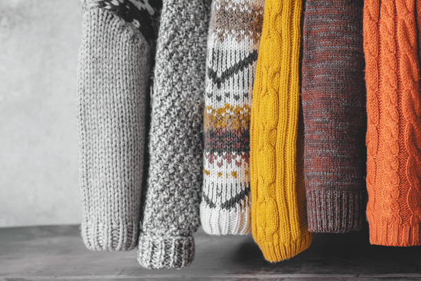 Sleeves of knitted sweaters in an autumn palette hang on a gray background. used sweaters. Ecological and sustainable fashion. . High quality photo - Photo, Image