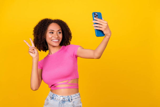 Photo of nice lovely girl make selfie hand fingers demonstrate v-sign isolated on yellow color background. - Foto, afbeelding
