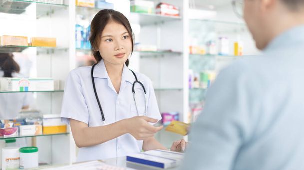 Credit card payment, Male patient pays by credit card to a pharmacist in a pharmacy, Get service at a community pharmacy , Pharmacist or cashier scanning medicinal products at checkout. - Photo, Image