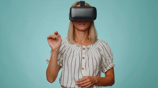 Вышел стильная женщина с использованием футуристической технологии виртуальной реальности VR шлем гарнитуры приложение для игры моделирования 3D 360 видео рисования игры. Молодая взрослая девушка на фоне синей студии. Люди искренние эмоции - Фото, изображение