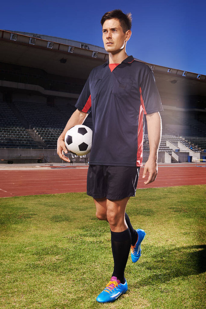 Hes dedicated to his sport. a young footballer standing on a field holding a ball - Foto, Imagen