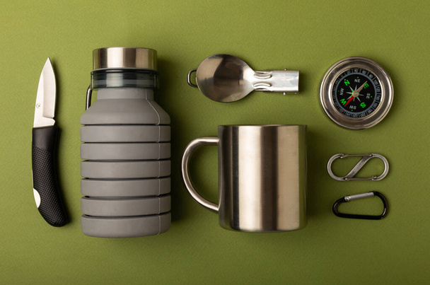 Set of tourist equipment on an olive background. EDC set flat lay. Camping plate, mug, bottle, spoon and compass. Flat lay. Top view. Space for copy.Tourist concept. Leisure. - Φωτογραφία, εικόνα