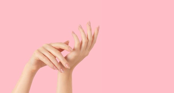 Hands of a beautiful well-groomed with feminine beige nude marble design nails gel polish on a pink background. Manicure, pedicure beauty salon concept. - 写真・画像