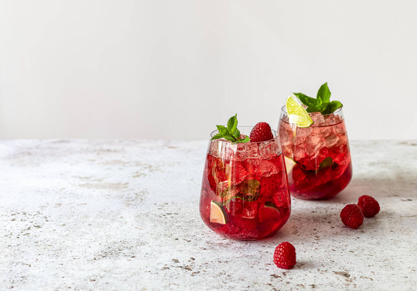 Fresh summer lemonade with raspberry, lime, soda water, and ice in glasses. Cold refreshing drink, cocktail or mocktail. - Foto, Bild