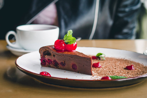 Una tazza di caffè con una torta al cioccolato brownie con ciliegie e menta. Dolce? dessert di hocolate in un caffè. Ricette dolci fatti in casa - Foto, immagini