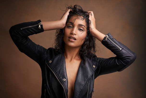 Her style is leather. Studio shot of an attractive young woman in a leather jacket against a brown background - Photo, Image