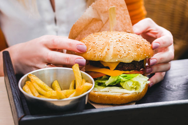 Ruce drží čerstvý lahodný burger s hranolky na černém dřevěném stole - Fotografie, Obrázek