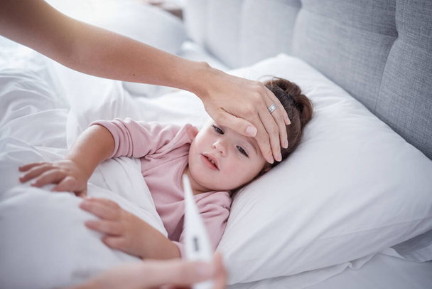 Άρρωστος, ιός και πυρετός παιδικό υπνοδωμάτιο με τη μητέρα αίσθημα ζεστό μέτωπο, θερμόμετρο θερμοκρασία και την υγειονομική περίθαλψη αποτελέσματα των δοκιμών πρόβλημα. Νεαρό κορίτσι ξεκουράζεται στο σπίτι για ιατρικά συμπτώματα και κίνδυνο covid. - Φωτογραφία, εικόνα