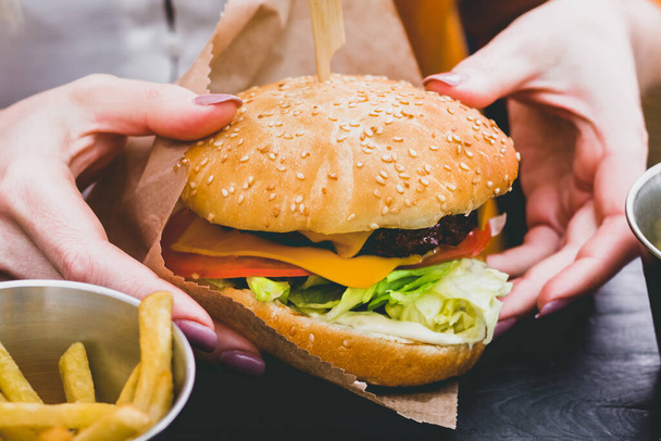 Női kéz kezében friss finom burger sült krumplival a fekete fa asztalon - Fotó, kép