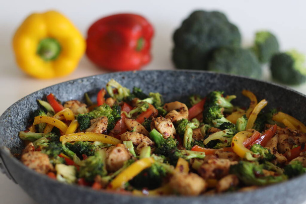 Stir fried vegetables with chicken in frying pan. Air fried chicken cubes tossed with sauteed bell peppers and broccoli. Shot along with broccoli bunches and bell peppers around on white background - Photo, Image