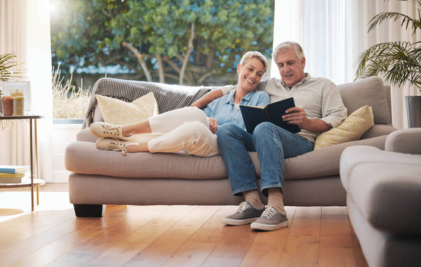 Retirement senior couple with photo album book on sofa together in summer house for vacation holiday. Happy elderly woman or people relax on couch in living room reading, talking of marriage history. - Foto, Imagem
